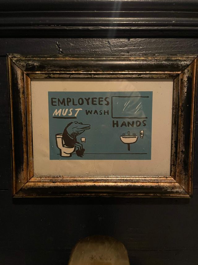Framed teal sign showing a cartoon alligator washing its hands at a sink, at Cozy Royal in Brooklyn