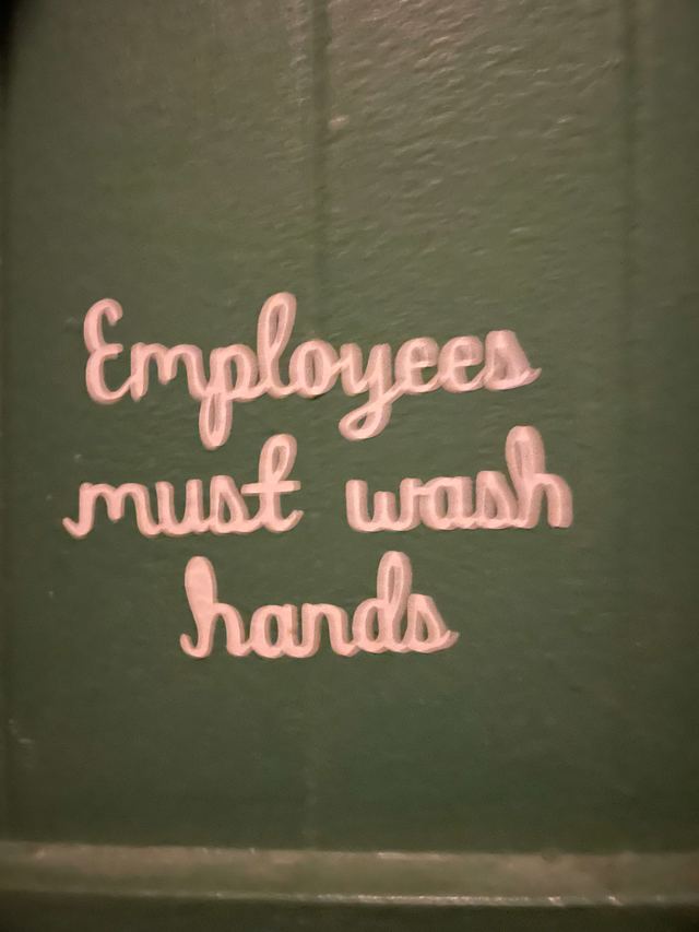 Pink cursive letters mounted on a dark green bathroom wall, reading “Employees must wash hands”