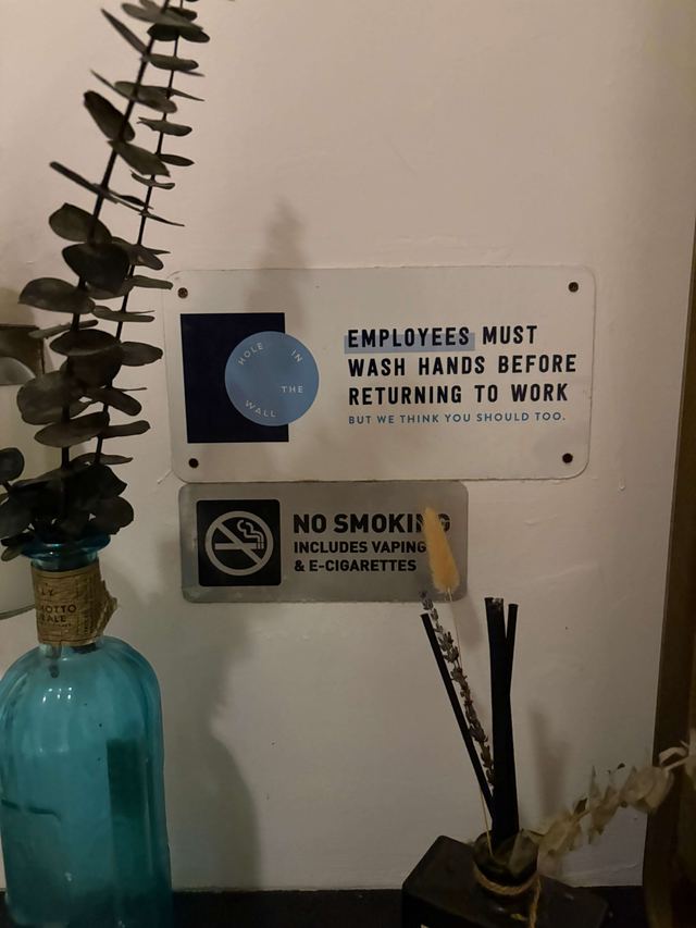 Sign at Hole in the Wall in Brooklyn adding “but we think you should too”, beside a no smoking sign