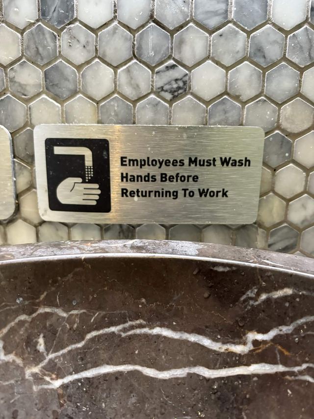 Brushed steel sign on grey hexagonal mosaic tile above a marble sink at Mission Ceviche in Manhattan