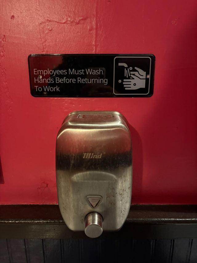 Black sign on a red wall above a stainless steel soap dispenser at Gonzalez y Gonzalez in Manhattan
