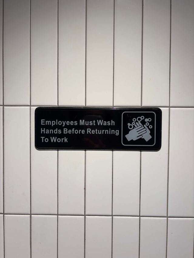Black sign with a hand-washing pictogram on white subway tile at NADC Burger in Manhattan