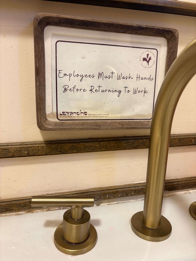 Handwritten sign in a stone frame above a brass faucet at Levantine in Brooklyn